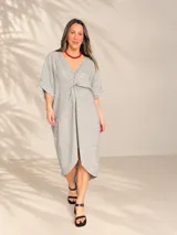 Vestido midi de lino color beige, con diseño oversize, escote en V y detalle de nudo drapeado en el frente. Posee mangas cortas amplias con dobladillo y corte asimétrico, siendo más largo en la parte trasera.