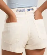 Short slim de cintura alta color blanco off-white, confeccionado en sarga de algodón con trabillas, bolsillos y cierre tradicional. Incluye un cinturón estilo pañuelo estampado.