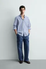 Camisa de corte regular fit confeccionada en tejido de algodón, con diseño de rayas verticales en azul y blanco. Presenta cuello solapa con botones, cierre frontal de botones, manga larga con puños abotonados y un bolsillo en el pecho.