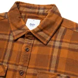 Camisa de franela marrón a cuadros con dos bolsillos frontales con solapa abotonada, de manga larga y corte clásico.