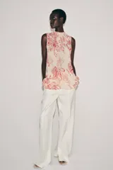Top sin mangas confeccionado en hilatura de viscosa, con cuello redondo y cierre en la espalda con abertura y botón. Presenta un diseño con estampado paisley a contraste en color rojo sobre fondo beige.