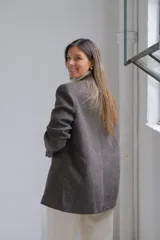 Blazer de corte sastrero en color gris oscuro con textura jaspeada. Presenta solapas clásicas, cierre frontal de doble botonadura y un bolsillo superior con detalle de pañuelo decorativo.
