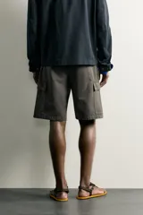Bermuda cargo color verde militar de corte relaxed fit, confeccionada en tejido de algodón. Cuenta con bolsillos laterales con solapa en las perneras, trabillas en la cintura con ajuste lateral y cierre frontal con cremallera y botón.