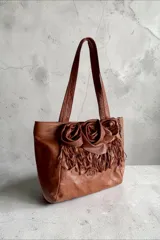 Cartera shopper de cuero color marrón terra, con doble asa de hombro y diseño decorativo de tres flores de cuero y flecos en el frente.