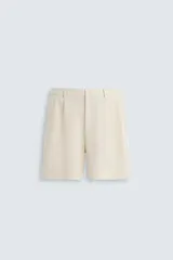 Bermuda de hombre color verde claro, de corte regular y tiro medio, con pinzas frontales, bolsillos laterales y bolsillos traseros de vivo. Cierre frontal con botón y cremallera.