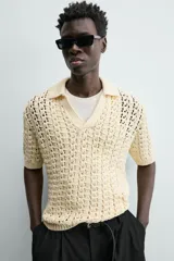 Polo de punto con estructura calada en color beige, confeccionado en algodón. Presenta un calce relajado, manga corta, cuello solapa con abertura frontal y terminaciones acanaladas.