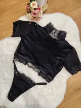 Conjunto de lencería compuesto por un top de cuello alto y una tanga, confeccionados en terciopelo negro con detalles de encaje y microtul. El top presenta mangas cortas con terminaciones en encaje y el borde inferior decorado con una cinta y encaje. La tanga es regulable y combina la textura del terciopelo con bordes de encaje.