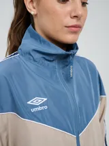 Campera cortaventos Umbro de diseño colorblock en tonos celeste, beige y azul marino, con cuello alto, cierre frontal y bolsillos laterales.