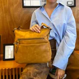 Bandolera de cuero sintético color mostaza, con dos bolsillos frontales con cierre, apertura superior con cierre, división interna y bolsillo trasero con cierre. Incluye correa larga regulable combinada en tonos mostaza y beige.