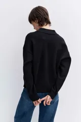 Sweater de punto negro con cuello polo y cierre frontal de botones, de manga larga y calce holgado.