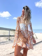 Camisero corto de manga tres cuartos, con cuello camisero y botones frontales. Presenta un estampado botánico en tonos marrón óxido y blanco, con dos bolsillos cuadrados de color beige liso en el pecho.