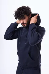 Buzo con capucha y bolsillo frontal tipo canguro, confeccionado en tela de felpa, con cordones ajustables en el cuello y puños elásticos.