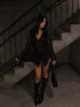 Vestido corto de tul negro con transparencias, escote en V con detalle de encaje, mangas largas acampanadas y falda con volados asimétricos.