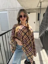 Poncho beige con estampado a cuadros en tonos marrón, negro y rojo, con diseño asimétrico y escote redondo.