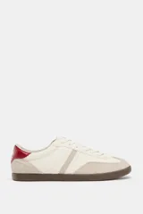 Zapatillas deportivas de mujer, estilo retro de bajo perfil, en tonos blanco hueso y beige claro. Presentan texturas mixtas en el cuerpo (piel granulada y gamuza) y un detalle en el talón de material rojo con textura de cocodrilo. La suela es de goma marrón oscura.