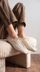 Zapato acordonado tipo oxford de cuero color off-white, con punta cuadrada, costuras decorativas y cordones finos al tono.