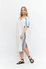 Túnica blanca de lino con corte oversized, escote en V, cierre con botones y mangas cortas. Presenta bordados geométricos azules en hombros y laterales.