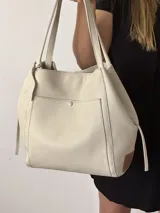 Bolso tipo tote de cuero color beige con doble asa de hombro y bolsillo externo con botón metálico.