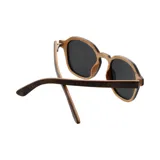 Lentes de sol con armazón de madera con acabado veteado y cristales oscuros. Presentan un diseño de marco redondeado con detalles metálicos en las esquinas.