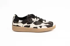 Zapatillas de cuero con acabado de pelo natural y estampado de manchas tipo vaca en blanco y negro. Presentan cordones negros y suela plana de goma en color tostado con costura visible.