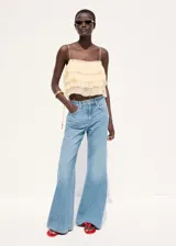 Pantalón de mezclilla de tiro medio con diseño acampanado estilo flare, trabillas para cinturón y clásico diseño de cinco bolsillos con cierre frontal de botón y cremallera.