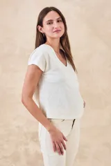 Remera blanca de algodón con escote en V y mangas cortas. Presenta un diseño estampado o bordado en negro de estilo tribal o geométrico en los laterales y mangas.