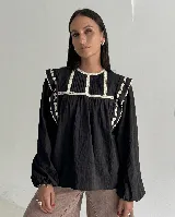 Blusa negra de algodón con cuello redondo, mangas largas con puños elásticos y detalles de puntilla y bordados florales en los hombros.