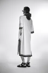 Túnica blanca de corte recto con cuello en V y mangas 3/4. Presenta detalles de ribete negro en cuello, mangas y ruedo.