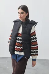Chaleco puffer negro con diseño acolchado, capucha desmontable y cierre frontal. Cuenta con cordones ajustables en la cintura y bolsillos laterales.
