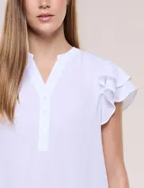 Blusa de gasa color azul, con cuello en V y abotonadura parcial. Cuenta con mangas cortas tipo mariposa con doble capa de volados y silueta fluida.