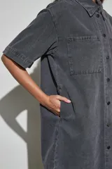 Vestido corto de denim azul oscuro, con cuello camisero, mangas cortas, cierre frontal de botones y dos bolsillos en el pecho.