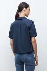 Camisa de algodón color beige claro, con cuello camisero, botones frontales y mangas cortas abullonadas con elástico en el puño.