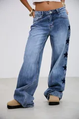 Pantalón de jean tiro medio con corte recto y holgado, presenta bordados de estrellas oscuras a lo largo de los laterales externos.