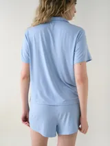 Camisa de manga corta para dormir de color rosado, confeccionada en viscosa. Presenta botones frontales, cuello con solapa, bolsillo en el pecho y ribetes a tono.