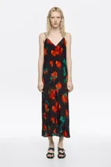 Vestido midi de corte recto con escote en pico, tirantes finos dobles y cierre frontal con botones. Presenta un estampado floral con flores rojas y toques verdes sobre fondo negro.
