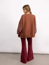 Buzo de algodón color negro con cuello redondo, mangas largas y bordado floral XL en color cobre en las mangas. Presenta un diseño holgado y cómodo.