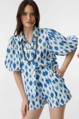 Short de lino blanco con estampado floral azul, de tiro alto, con bolsillos laterales y cierre frontal con gancho metálico.