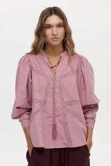 Blusa de algodón liviano color blanco, con detalles de puntilla en el frente, cuello mao con escote en V, cordón colgante y mangas largas abullonadas con puños ajustados.