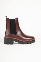 Bota Chelsea color bordó de cuero sintético, con punta redonda, elástico lateral negro y suela track color negro.