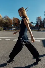 Vestido corto de cuello subido y sin mangas, confeccionado en tejido satinado. Presenta un detalle de fruncido lateral con abertura frontal y aplicación de encaje en el bajo.