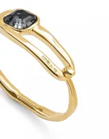Pulsera rígida dorada con cristal facetado negro en el centro.