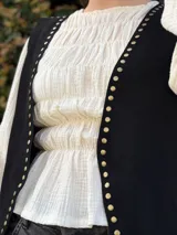 Chaleco de cuero negro con tachas metálicas doradas en los bordes frontales.