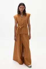 Pantalón de lino color marrón, de corte ancho con tiro medio-alto, tablas delanteras y elástico en la parte trasera.