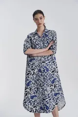 Vestido camisero midi con estampado floral en tonos azul, blanco y negro. Tiene cuello camisero, mangas 3/4 y abotonadura frontal parcial.