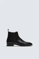 Bota estilo Chelsea de cuero negro con punta fina, paneles elásticos laterales y tirador trasero.