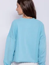 Buzo celeste de tela deportiva con mangas largas caídas y terminación al corte en los bajos.