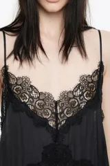 Vestido largo negro con caída fluida, escote en V con tirantes finos y detalles de encaje floral en el escote y el pecho.