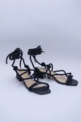 Sandalias doradas con tiras de cuerda para atar al tobillo.