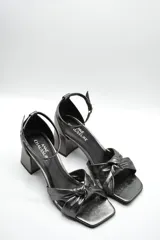 Sandalia de tacón medio ancho con diseño de nudo frontal y pulsera ajustable al tobillo con hebilla metálica.