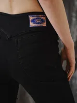 Pantalón de jean negro elastizado, tiro a la cintura, con calce ajustado y apertura tipo flare en las piernas. Presenta recortes curvos y costuras expuestas con terminación desflecada.